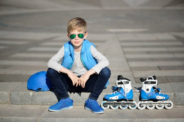 Ung pojke sitter nära grå vägg med inline rullskridskor och alla skydd på utomhus skatepark — Stockfoto