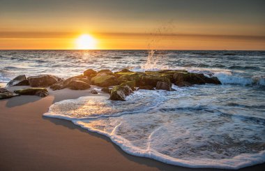 Köpüklü su plajda güneş doğarken NJ 'deki Beach Haven' da sahili ıslatırken dalgalar kayaların üzerine sıçrıyor.