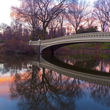 Doğal kış gündoğumu yay Bridge yakınındaki New York Central Park içinde. Sakin göl suları ve Manhattan gökdelen üzerinde olan arka plan yansıması ile köprü.