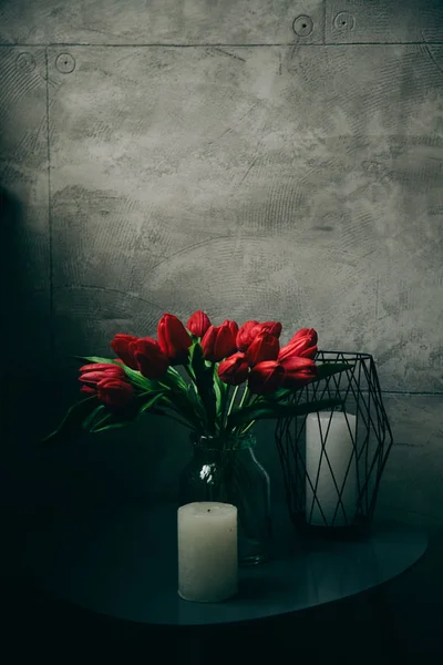 红郁金香在玻璃杯里 灰色墙边的桌子上的花 — 图库照片