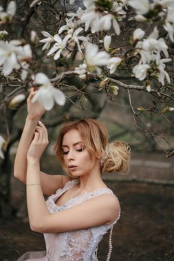 parkta erken ilkbaharda. Beyaz güzel yemyeşil elbiseli kız. sarışın kız akşam saç modeli ve etkileyici makyaj ile. Manolya çiçek bir kız