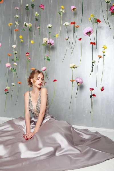 beautiful young girl in luxury silver dress. hanging colourful flowers. blonde with bridal hairstyle. idea for wedding decor. spring portrait for young lady
