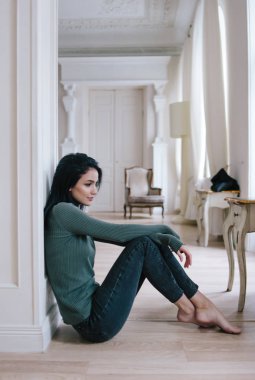 genç güzel esmer parlak makyajlı. bir kız bir yeşil kazaklı bir beyaz oda katta oturur.