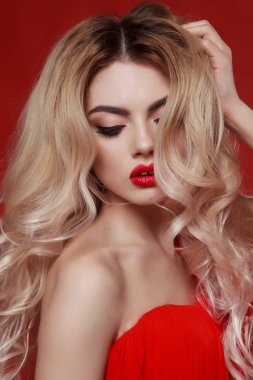 yakın çekim portre zarif kadın kırmızı moda elbise. uzun sarı saç. genç kadın kırmızı zemin üzerine. modeli kıvırcık saçlı ve kırmızı dudak makyaj