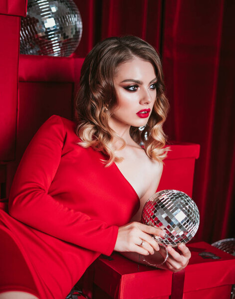 блондинка гламурная женщина рядом с красными подарками. представляет концепцию. молодая красивая женщина позирует в красном платье. девушка с красными губами макияж. Голливуд кудри прическа
. 