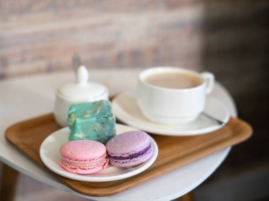 Masada badem kurabiyeli bir fincan kahve. Beyaz kapuçino ve pembe ve leylak kurabiyeli çay tabağı..