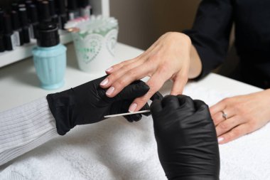 Tırnak bakımı. Güzel kadın elleri pembe arka planda pembe ojeli oje ile oje yapıyor. İş sırasında manikürcü. Kafkasyalı spa salonunda manikür yapıyor.