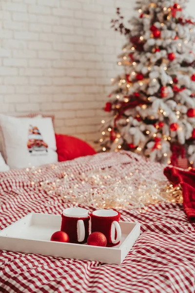 クリスマスの装飾でベッドの上の2つのカップ 赤と白の家の装飾自宅で居心地の良いクリスマスの概念 ベッドでクリスマスの朝食 — ストック写真