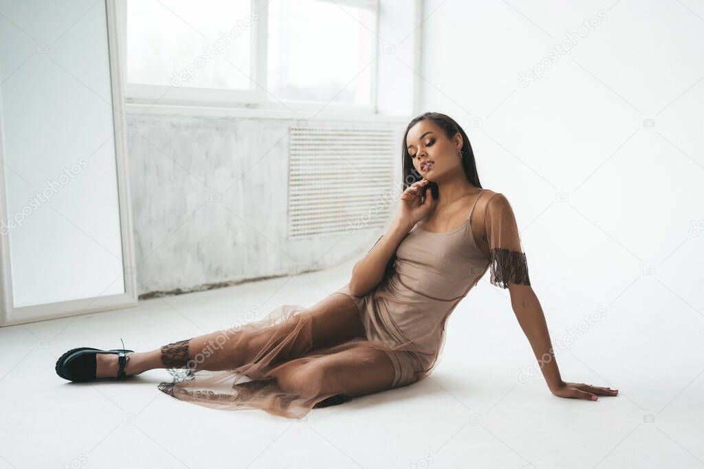 young beautiful african woman posing on white cyclorama. fashion model in beige lace dress and black boots. trendy outfit