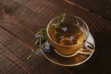 Kahverengi ahşap zemin üzerinde çay fincanı, bir fincan çay ve çiçek. Sağlıklı içecekler, organik çiçek çayı. arkaplan kopyalama alanı. Bitki çaylı cam bardak.