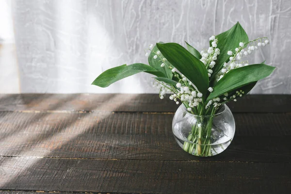 Lily of the valley flowers in glass vase, cement background, selective focus.Still life with a bouquet of white lilies of the valley in a glass vase on the table.