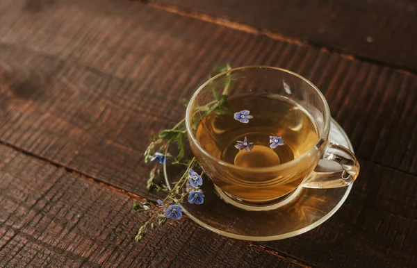 Cup of tea with a saucer and the flower,  on brown wooden background. Healthy drinks, organic flower tea. background copy space. glass cup with herbal tea