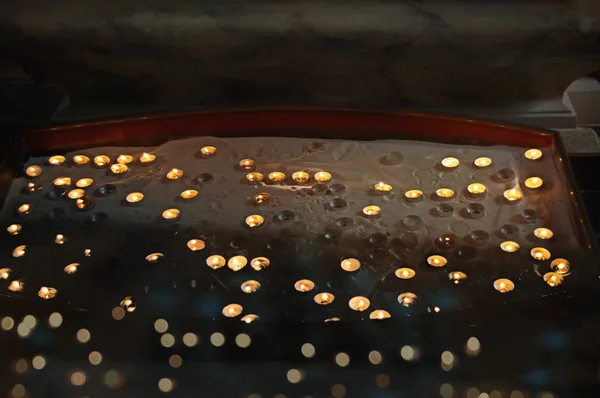 Muitas pequenas velas votivas em uma areia em uma caixa de suporte especial — Fotografia de Stock