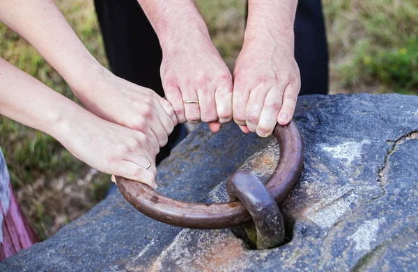 Kvinnan och mannens armar med vigselringar dra en stor metallring — Stockfoto