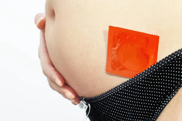 Pregnant woman holding her hand on a belly and a red condom — Stock Photo, Image