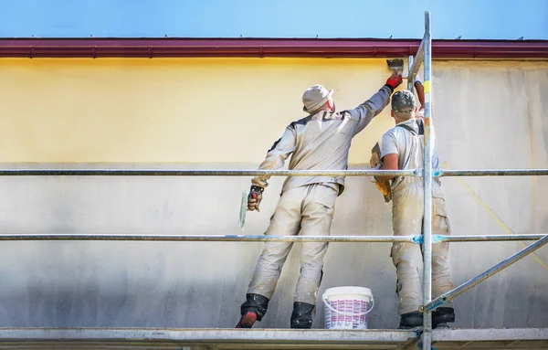 Two builders on safety scaffolding  make yellow decorative plast