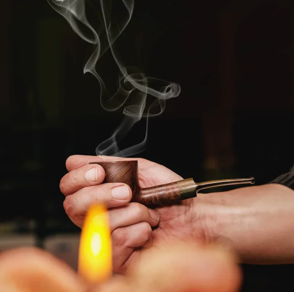 La mano dell'uomo che tiene la pipa con il fumo in uno sfondo scuro — Foto Stock