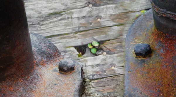 Zwei alte Schrauben behaupten eine rostige Metallkonstruktion an einem Holzsockel — Stockfoto