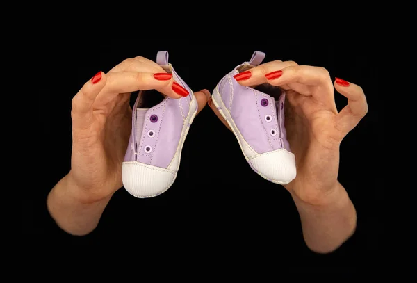 Vrouwenhanden houden twee baby schoenen op een zwarte achtergrond — Stockfoto