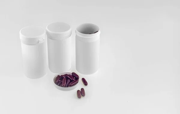 Three white  plastic jars and dark red medicine  capsules on a w — Stock Photo, Image