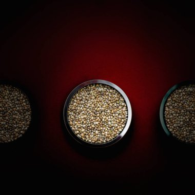 Koyu kırmızı arka planda metal plakalarda kenevir tohumu. Kapat..