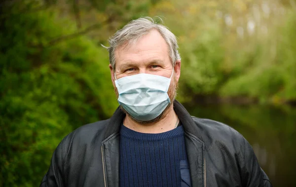 A happy man on a nature walk by the river in a medical mask rejoices at the end of the quarantine.