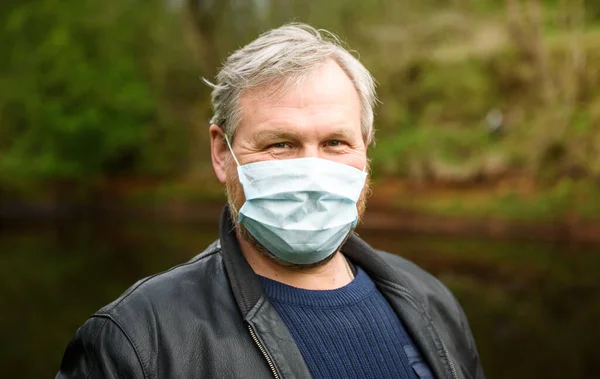 A happy man on a nature walk by the river in a medical mask rejoices at the end of the quarantine.