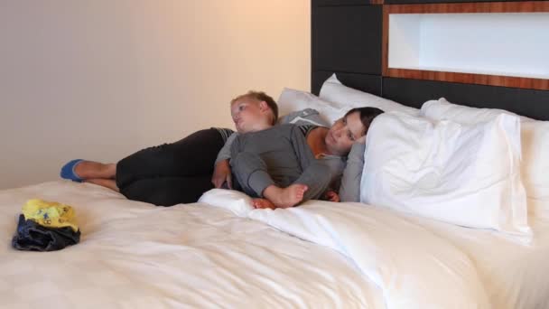 Мать и ее ребенок отдыхают в гостиничной кровати и смотрят телевизор — стоковое видео