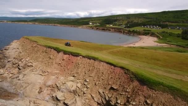 En bonde som klippa höet i sitt område på en ocean udde — Stockvideo