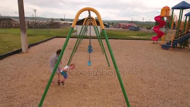 Mother and boy playing on a city park swing — Stock Video