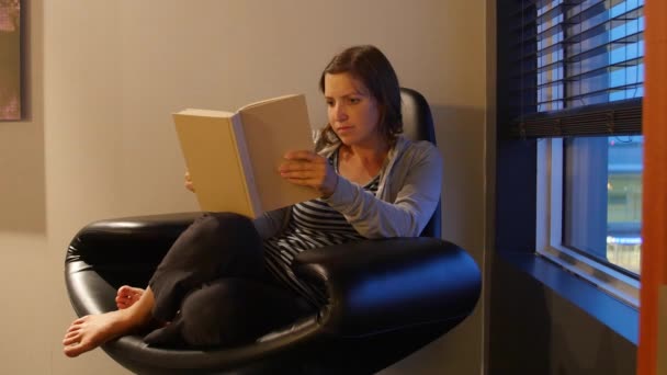 Eine Frau liest Buch im modernen Stuhl — Stockvideo