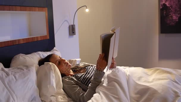 Жінка читає свою книгу в зручному ліжку — стокове відео