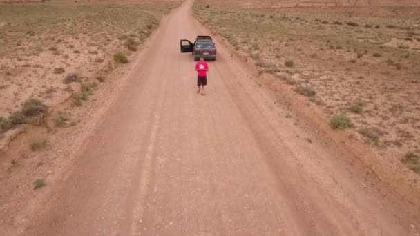 Hombre aterrizando su dron usando su control remoto en un camino del desierto — Vídeos de Stock