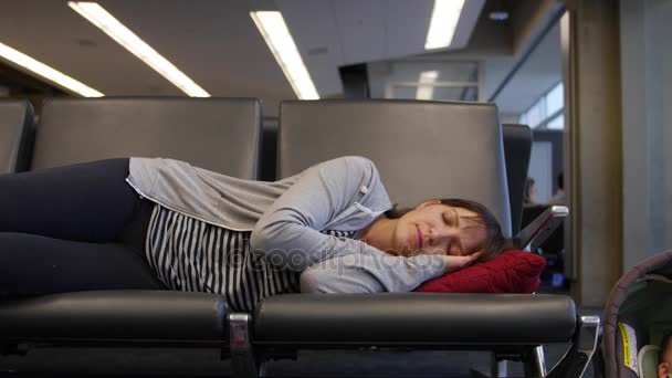 En trött kvinna sover på flygplatsen med baby — Stockvideo