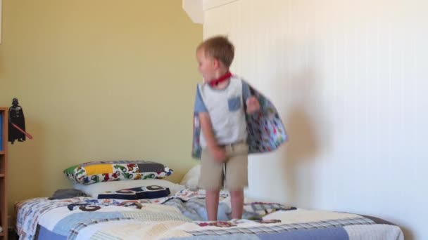 Een peuter met een cape springt op zijn bed — Stockvideo