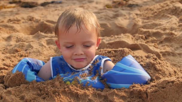 Jongen begraven in zand op strand — Stockvideo