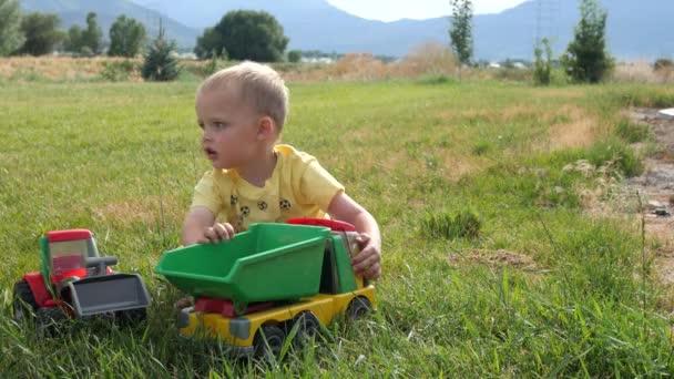 Niño juega con tractores y camiones fuera — Vídeo de stock