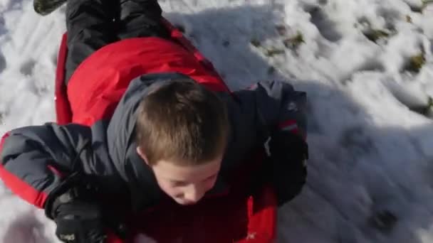Junge schlittert einen verschneiten Hügel hinunter — Stockvideo
