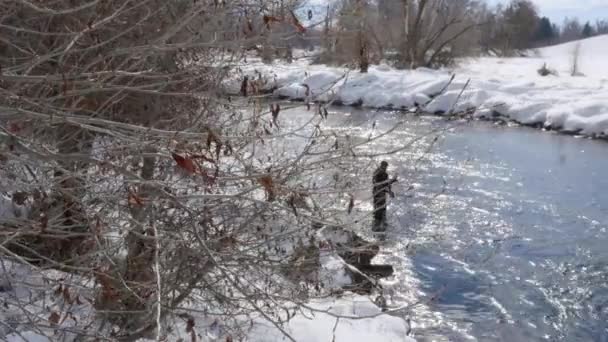 Человек рыбачит зимой в реке — стоковое видео