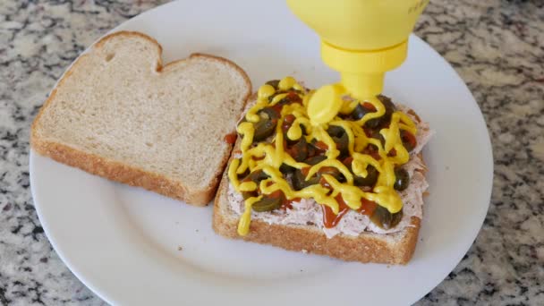 Человек кладет горчицу в сэндвич с тунцом — стоковое видео