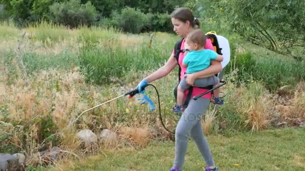 Mother with a toddler sprays weeds with weed killer — Stock Video