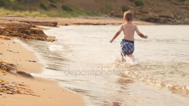 Chlapec, běh přes oceán na pláži — Stock video