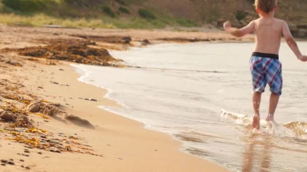 Chico saltando a través del océano en una playa — Vídeos de Stock