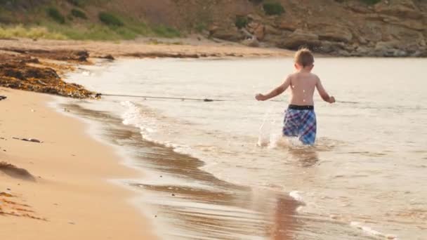 Menino pulando através do oceano na praia — Vídeo de Stock