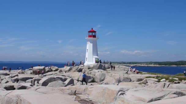 Turister går runt den granitklippor som omger Peggy's Cove lighthouse — Stockvideo