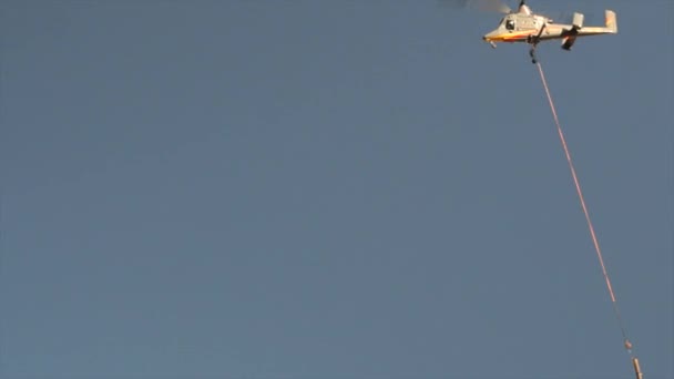 Un hélicoptère transportant un poteau téléphonique à travers les montagnes — Video