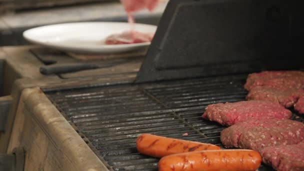 Een man kookt hamburgers en hotdogs op een barbecue — Stockvideo