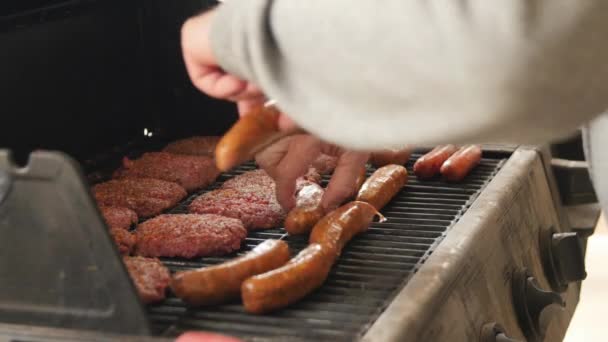 Een man seizoenen hamburgers en hotdogs op grill — Stockvideo