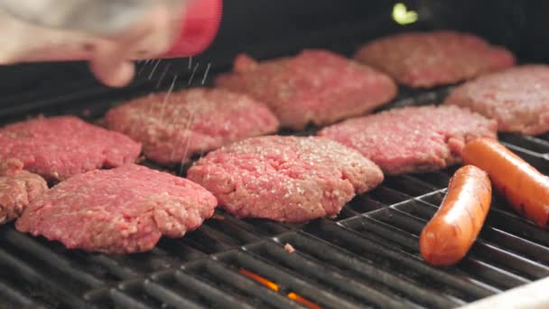 En mand krydrede hamburgere og hotdogs på grillen – Stock-video