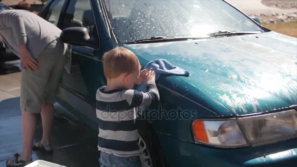 Un niño pequeño ayudando a la madre a lavar el coche — Vídeo de stock